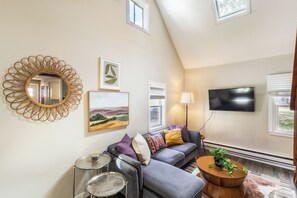 Un salon moderne avec un canapé gris, une table basse ronde en bois et un grand miroir au mur.