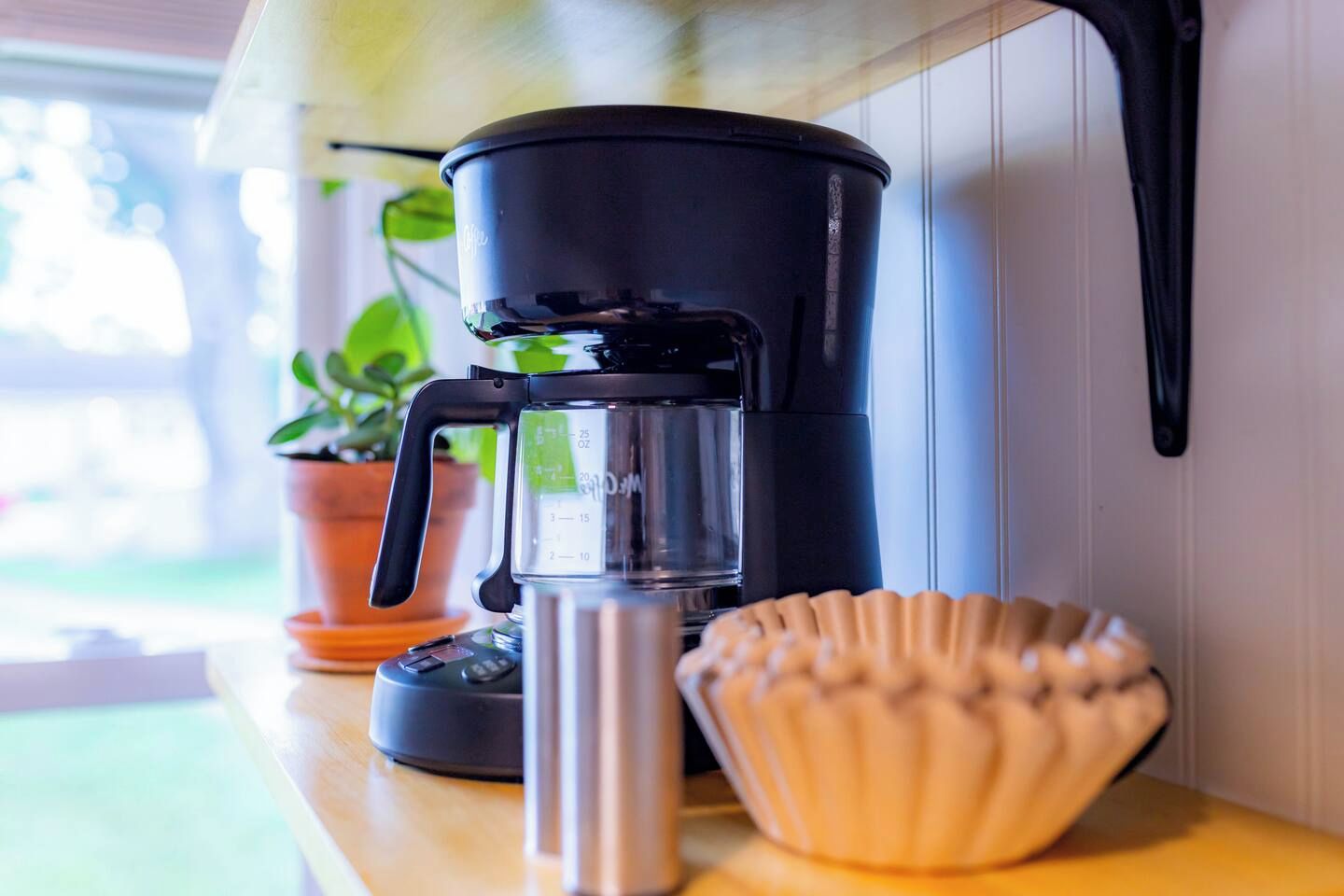 A coffee maker on a countertop with a measuring cup and a decorative shell.