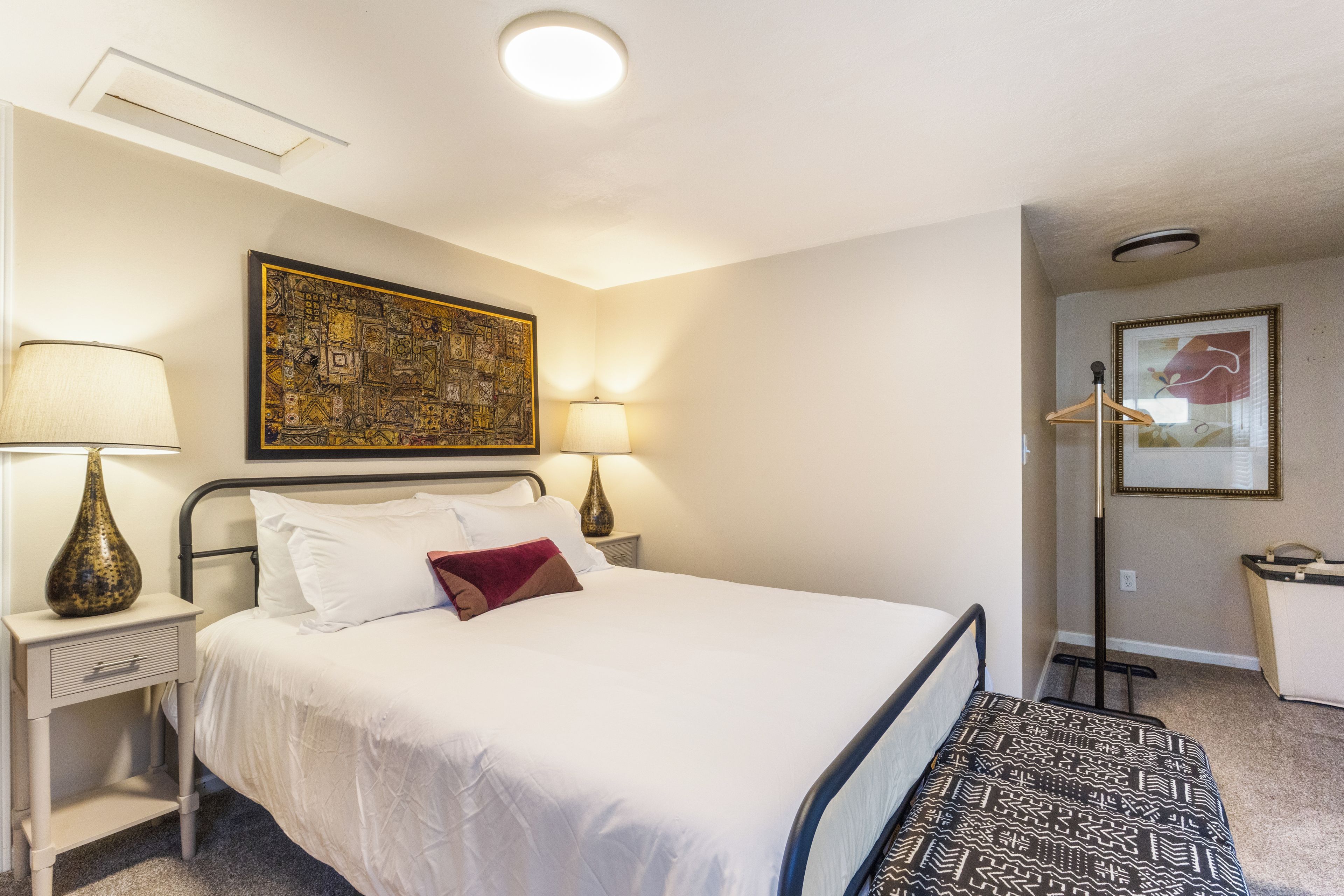 A hotel room with a bed, bedside lamps, a wall-mounted artwork, and a door leading to a bathroom.