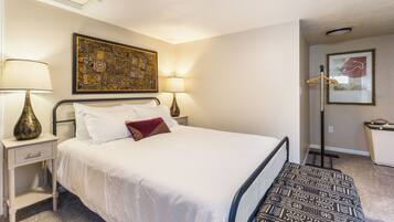 A hotel room with a bed, bedside lamps, a wall-mounted artwork, and a door leading to a bathroom.
