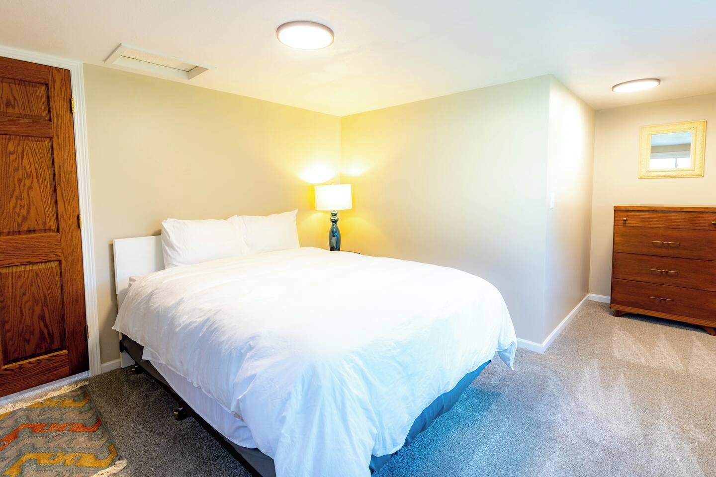 A bedroom with a bed, a dresser, a lamp, and a door.