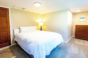 Une chambre à coucher avec un lit, une commode, une lampe et une porte.