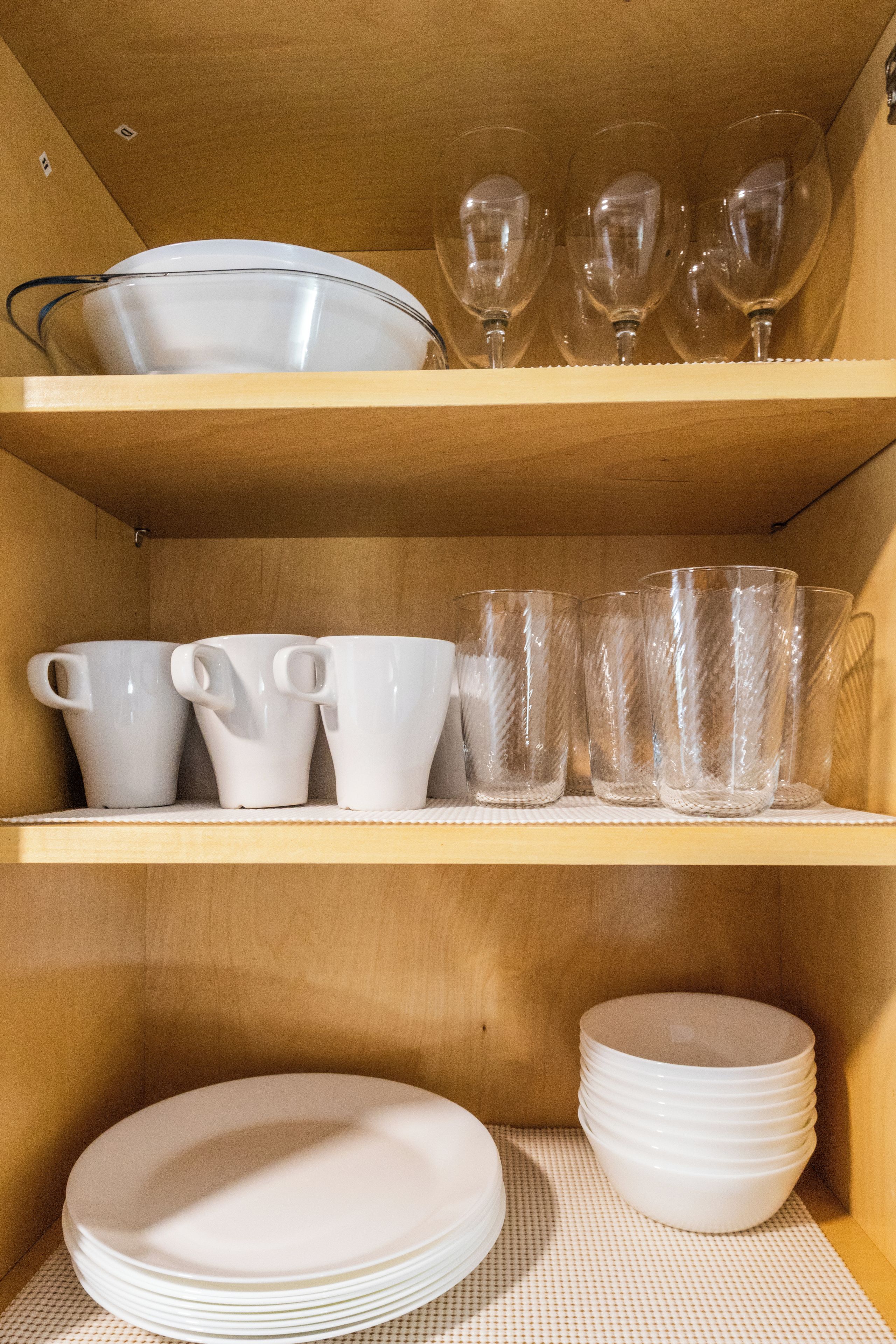 Une étagère en bois sur laquelle sont disposés des plats, des tasses et des verres en céramique blanche.