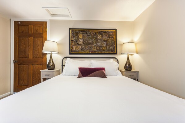 A hotel room with a large bed, two bedside tables, a wooden door, and a wall-mounted artwork.