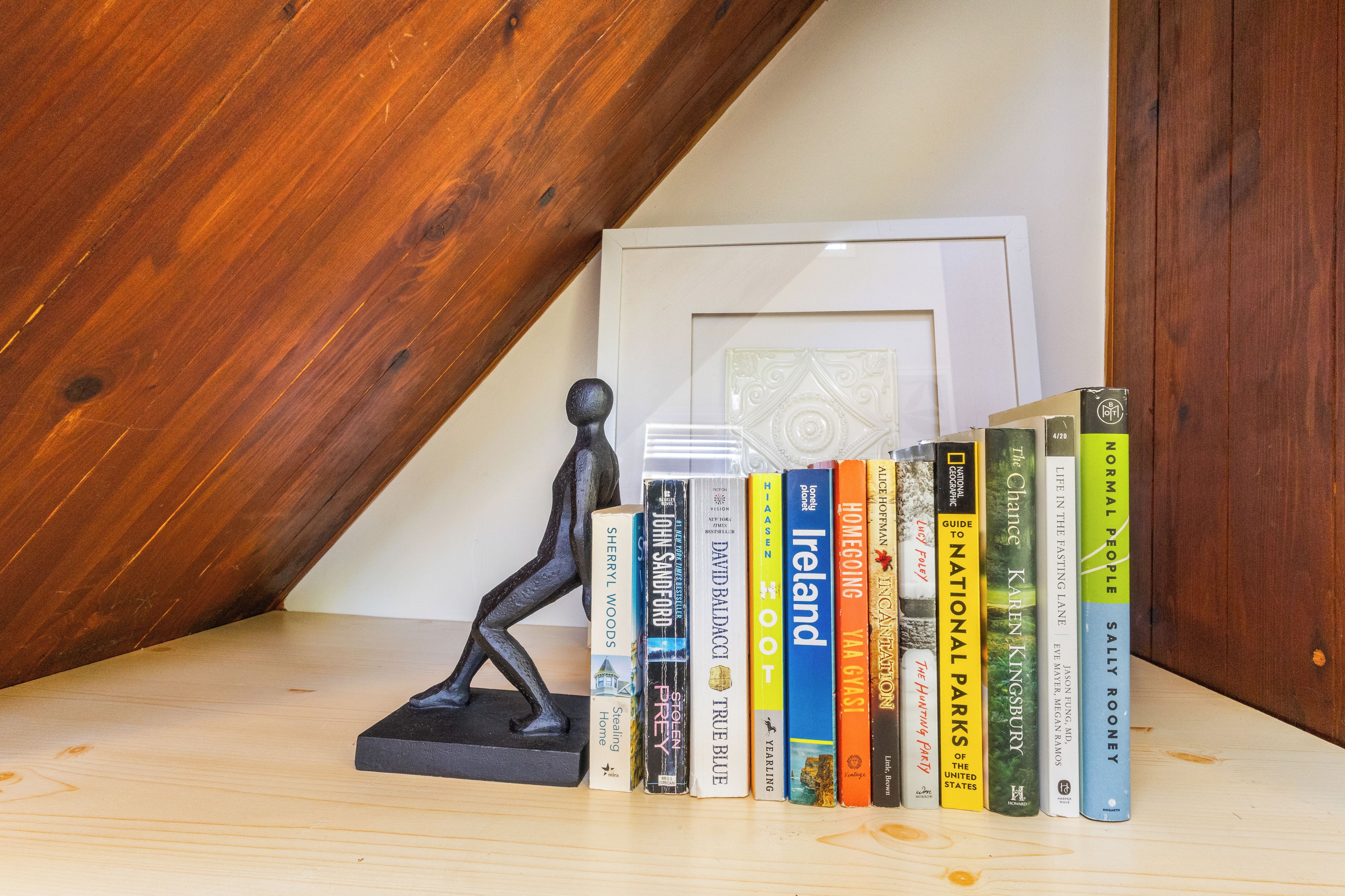 A wooden shelf with a black sculpture and a row of books.