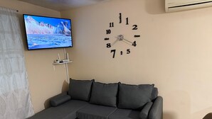 Ein Wohnzimmer mit einem grauen Ecksofa, einem flachbildfernseher an der Wand und einer Wanduhr.