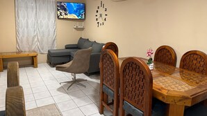 Ein Wohnzimmer mit einer Couch, einem Esstisch mit Stühlen, einem Fernseher und einer Klimaanlage.