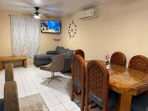 Ein Wohnzimmer mit einer Couch, einem Esstisch mit Stühlen, einem Fernseher und einer Klimaanlage.