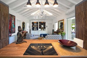 Ein modernes Wohnzimmer mit einem Holzesstisch, einer integrierten Kücheninsel und einer Sitzecke mit gemusterten Sofas.