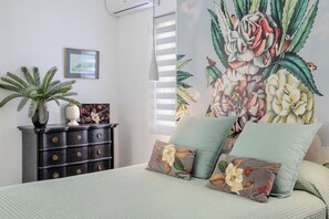 Ein Schlafzimmer mit einem Bett, einer Kommode, einer Zimmerpflanze und Wandmalerei.