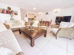 Una sala de estar con una amplia mesa de centro, sofás y una televisión.