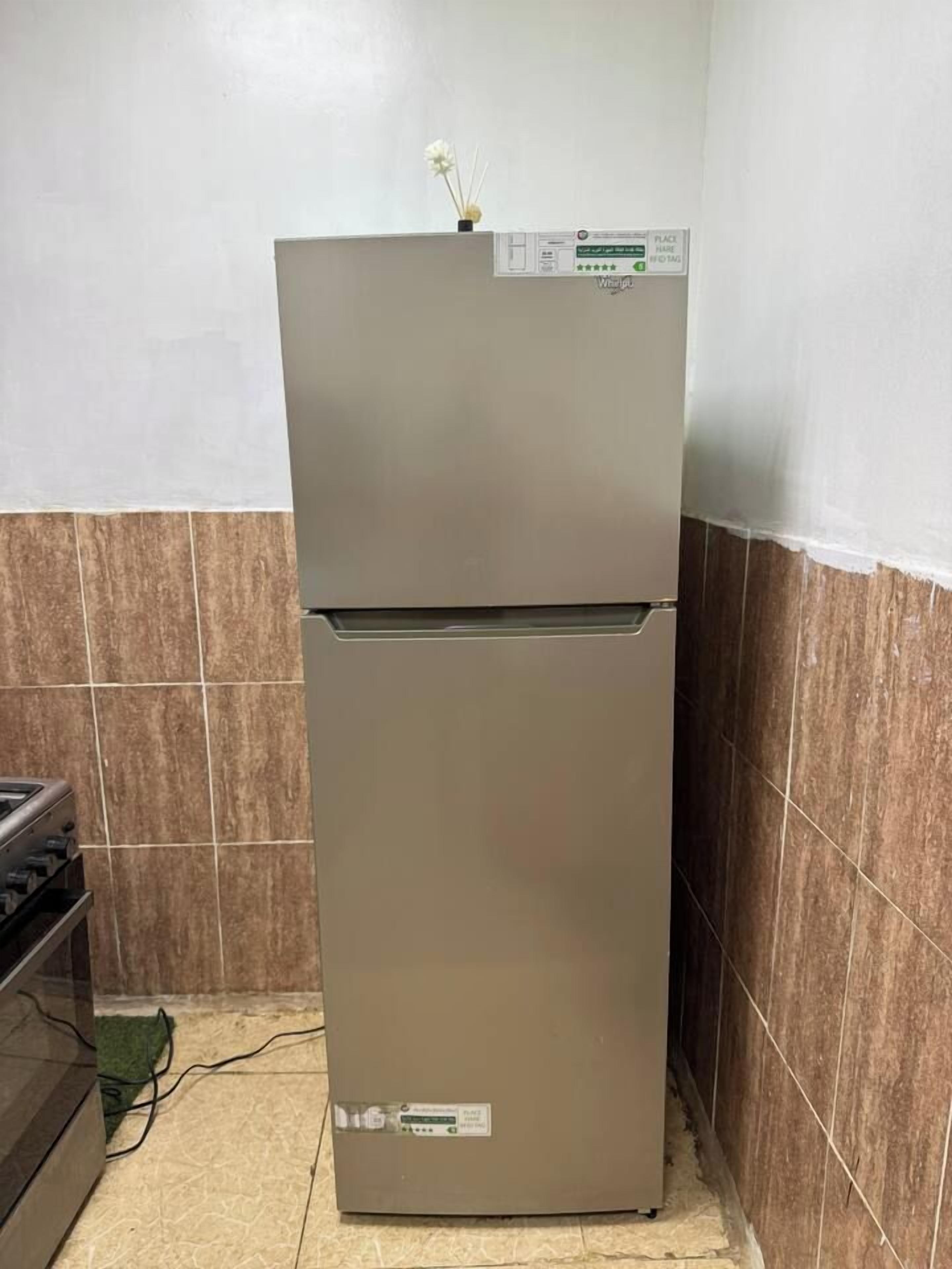 A kitchen with a stainless steel refrigerator, a stove, and tiled walls.