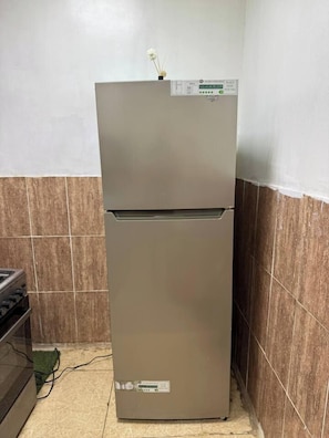 A kitchen with a stainless steel refrigerator, a stove, and tiled walls.