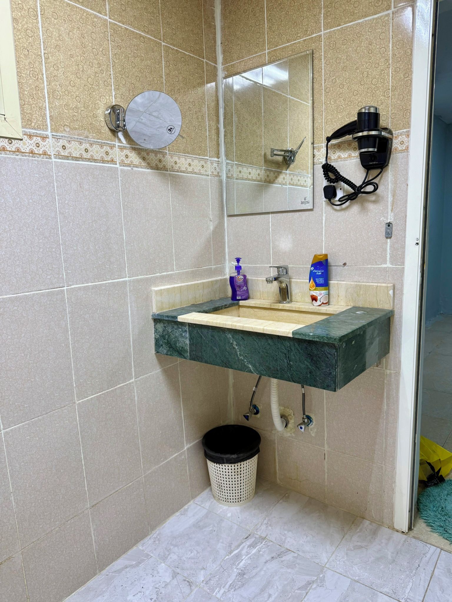Une salle de bain équipée d’un lavabo en marbre, d’un miroir, d’un sèche-cheveux et d’une poubelle.