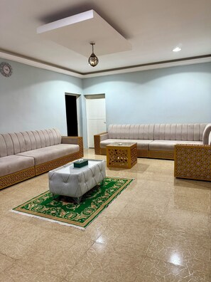 A spacious living room with a beige sofa, a matching armchair, a coffee table, and a patterned rug.