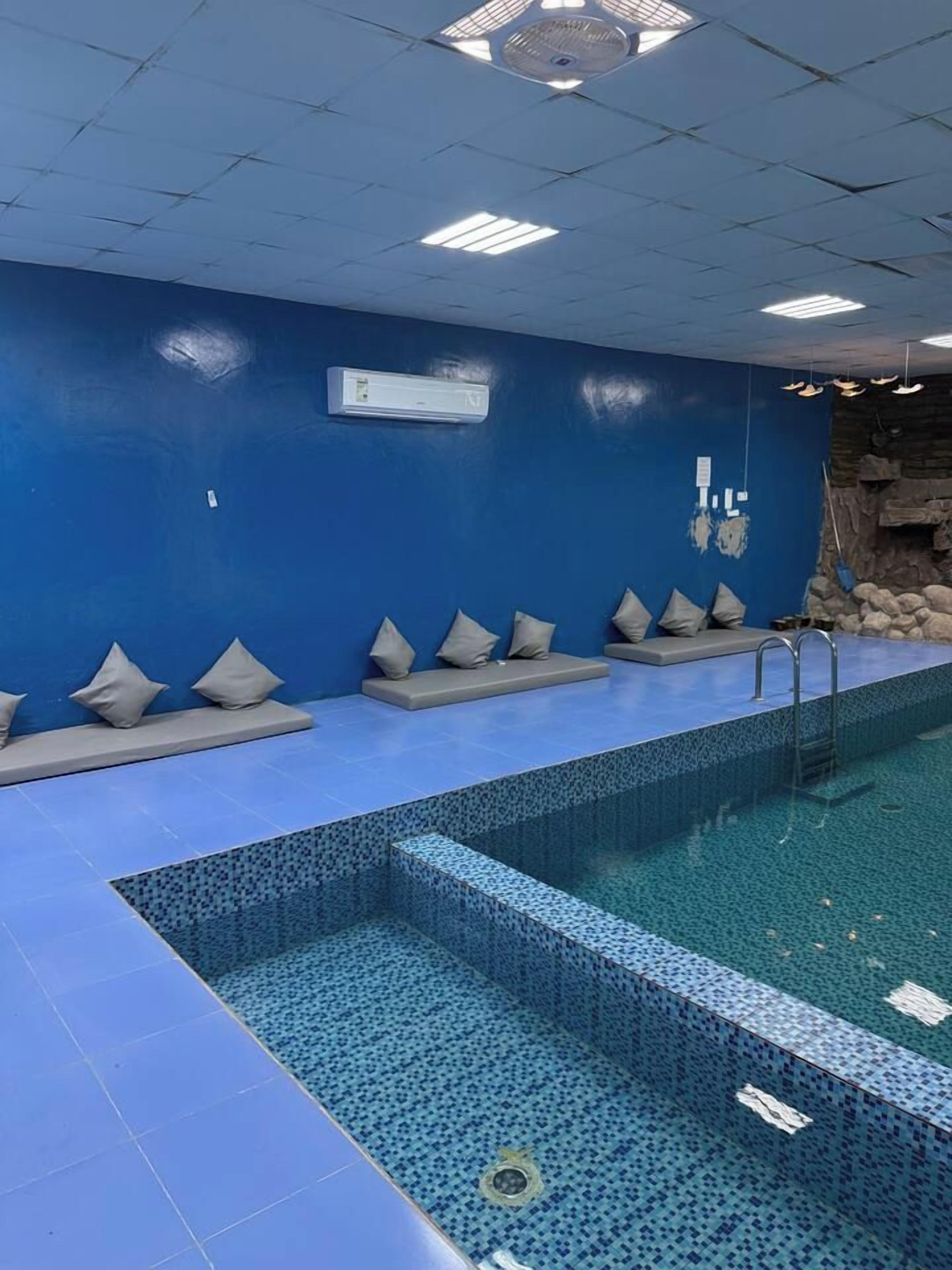 A swimming pool with a blue tiled floor and walls, a stone wall feature, and a ceiling fan.