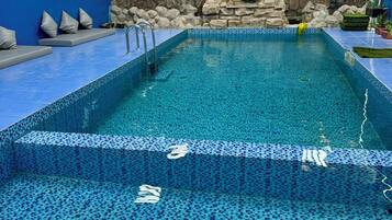 An indoor swimming pool with a stone wall backdrop, tiled flooring, and a blue color scheme.