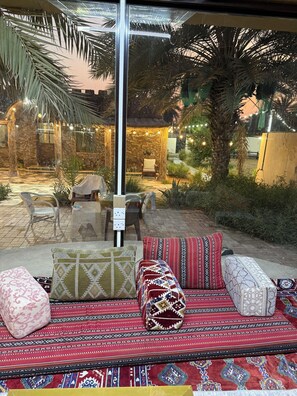 An outdoor seating area with patterned cushions, a stone wall, and palm trees.