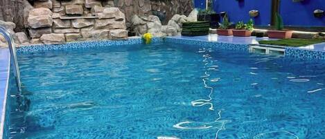 Una piscina interior d'aigua cristal·lina, una paret de pedra i una paret blava amb jardineres penjants.