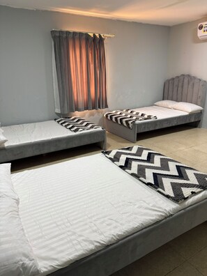 Ein Zimmer mit zwei Einzelbetten, einem Vorhangfenster und einer wandmontierten Klimaanlage.
