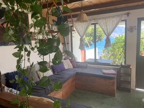 A room with a wooden bench, a sofa, and a hanging plant. There is a window with a view of greenery and a mountain. - Our Birdhouse - Relax & Swim - Your Peaceful Getaway (San Pedro La Laguna)