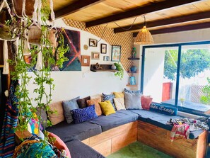 Een gezellige woonkamer met een inbouwkbank, een groot raam met uitzicht en diverse decoraties aan de muur.