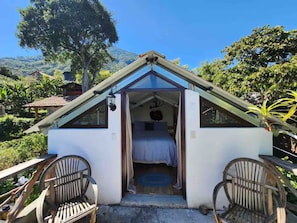 A small, single-room structure with a sloped roof, a bed, and two chairs. - Our Birdhouse - Relax & Swim - Your Peaceful Getaway (San Pedro La Laguna)