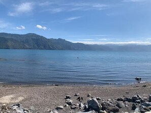 A rocky shoreline with a calm lake and distant mountains. - Our Birdhouse - Relax & Swim - Your Peaceful Getaway (San Pedro La Laguna)