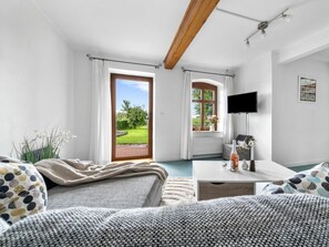 Ein Schlafzimmer mit einem Bett, einem Schreibtisch, einem Fernseher und Blick auf einen Garten durch eine Tür.