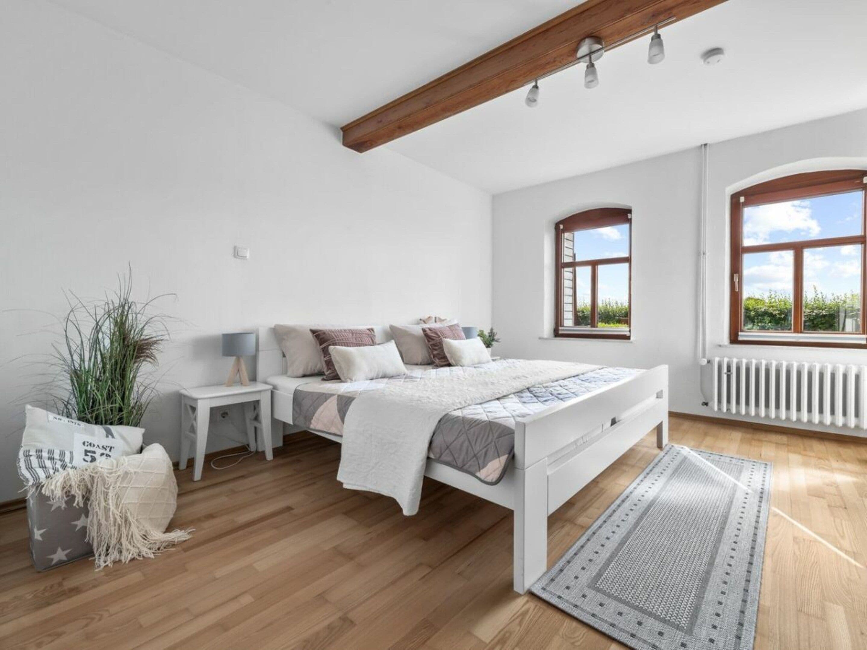 A bedroom with a bed, bedside tables, a radiator, a window, and a plant.