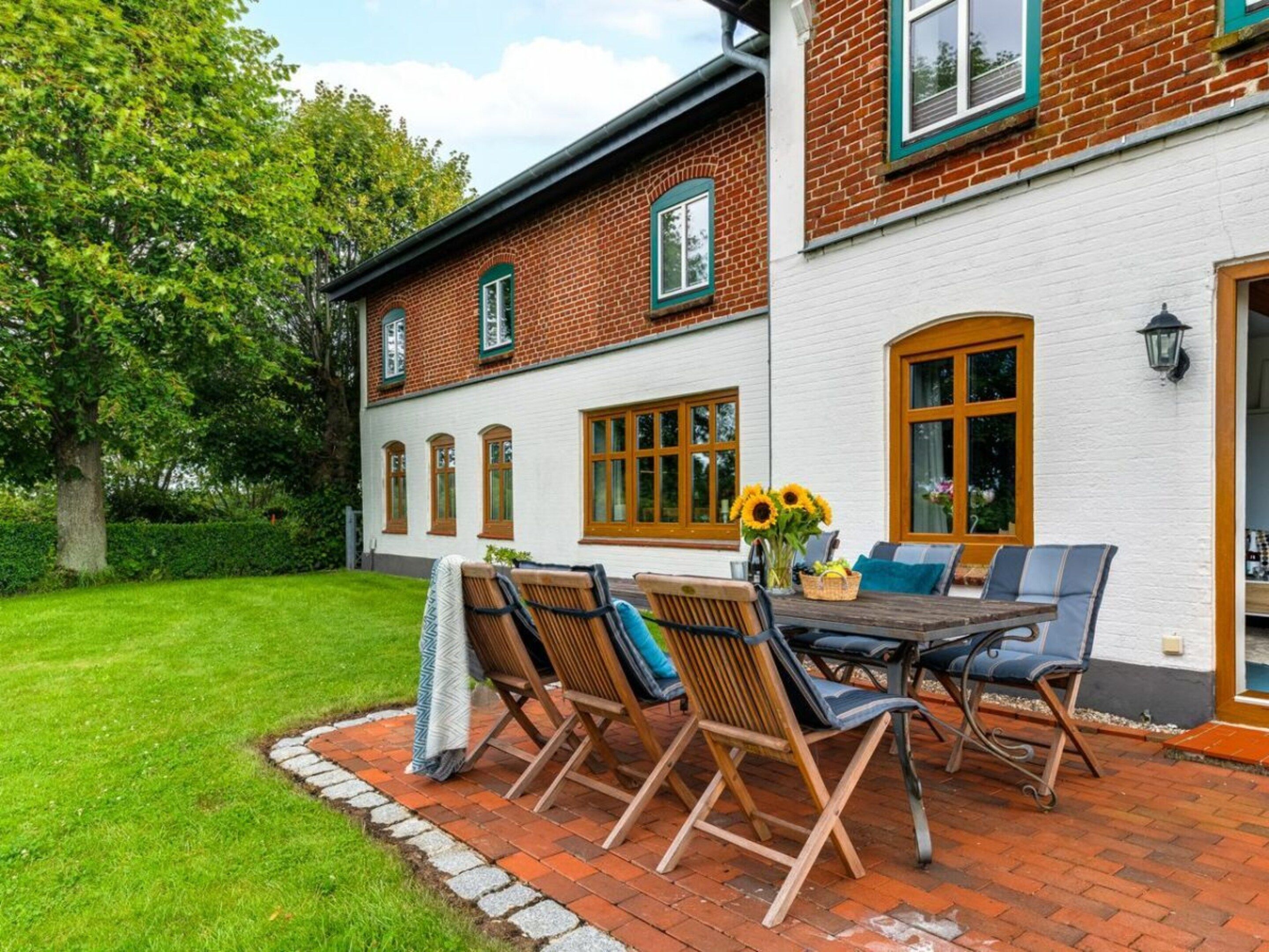 A brick house with a white exterior, a patio with a table and chairs, and a garden with a tree.