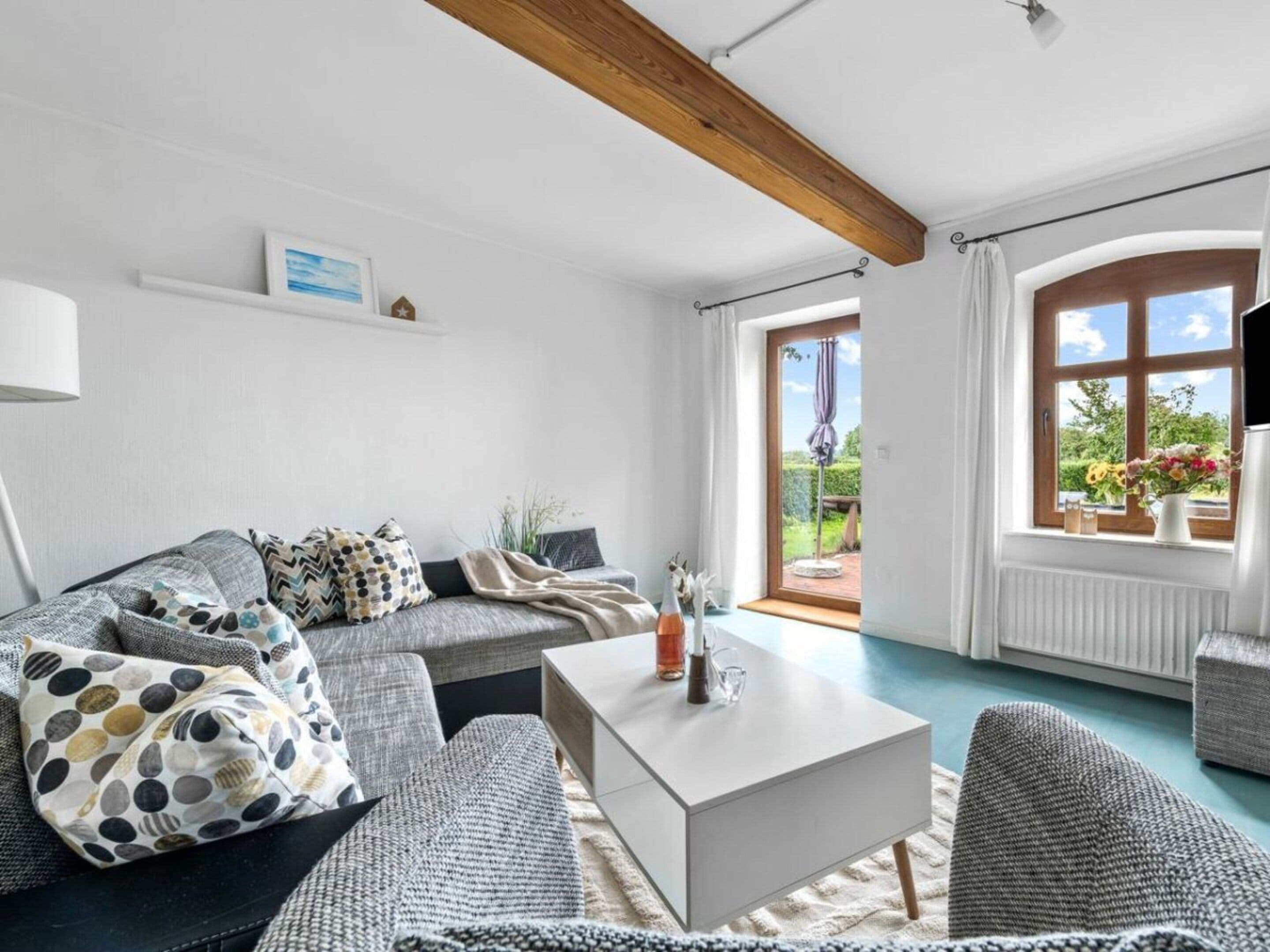 Un salon moderne avec un canapé gris, une table basse blanche et une vue sur l’extérieur grâce à une grande fenêtre.