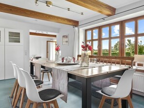 A modern dining area with a wooden table, white chairs, and a view of the outdoors through large windows. - Holiday Apartment With 1 Bedroom (Steinberg)