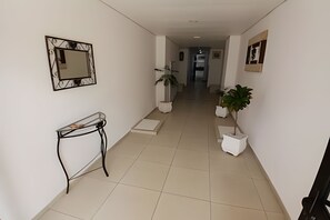 Un pasillo con espejo, una consola, plantas en macetas y una puerta al final.