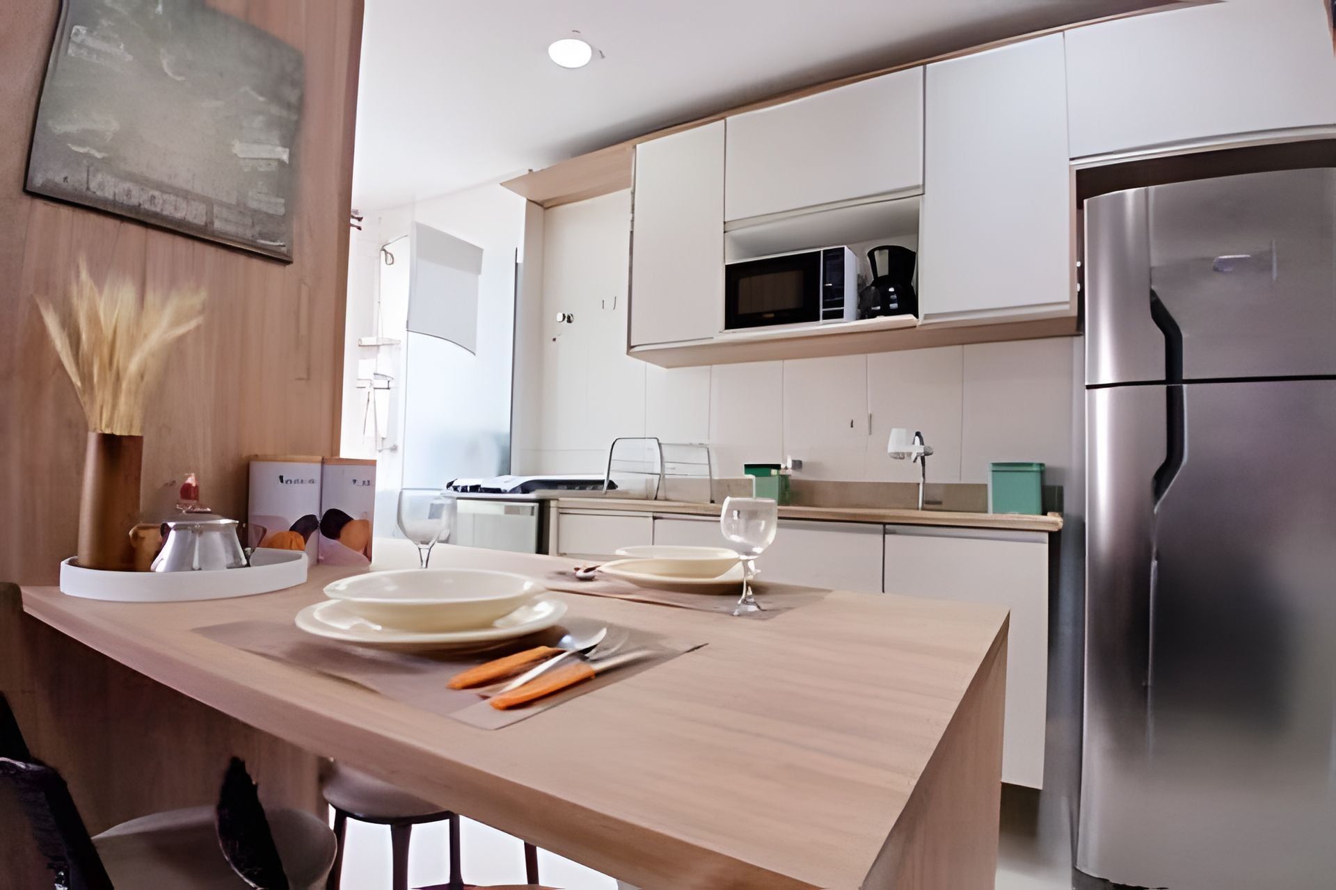 Una cocina moderna con armarios blancos, un refrigerador de acero inoxidable y una isla de madera con platos y cubiertos.