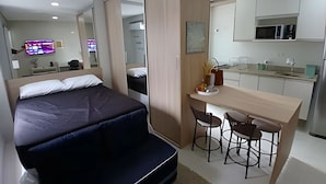 Un dormitorio con cama, un escritorio con dos sillas, un espejo y una kitchenette.