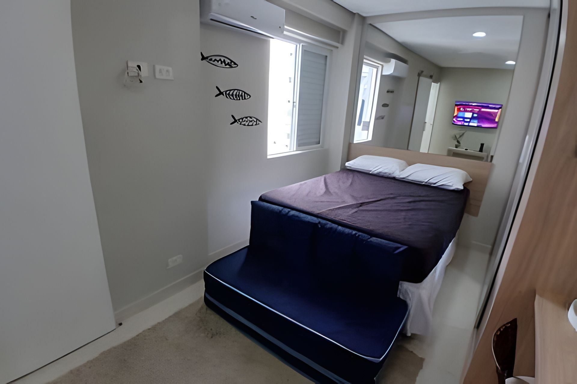 A bedroom with a bed, a window, and a wall-mounted TV.