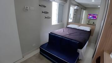 A bedroom with a bed, a window, and a wall-mounted TV.