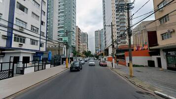 A street with tall residential buildings, a sidewalk, and parked cars.