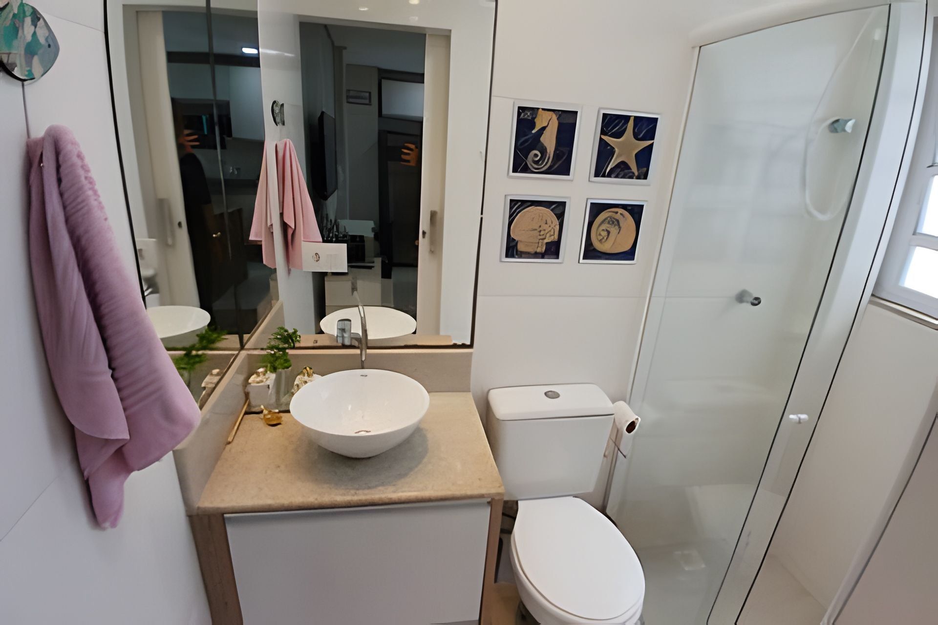 Un baño moderno con lavamanos, inodoro y ducha blancos. Hay cuadros enmarcados en la pared y una toalla colgando.