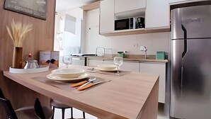 Una cocina moderna con armarios blancos, un refrigerador de acero inoxidable y un comedor con una mesa de madera lista para dos.