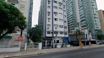 Un edificio residencial de varios pisos con balcones, una entrada protegida por un portón y un pequeño edificio comercial al frente.
