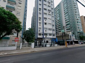 Un edificio residencial de varios pisos con balcones, una entrada protegida por un portón y un pequeño edificio comercial al frente.