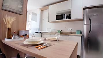 A modern kitchen with white cabinets, a stainless steel refrigerator, and a wooden island with diningware.
