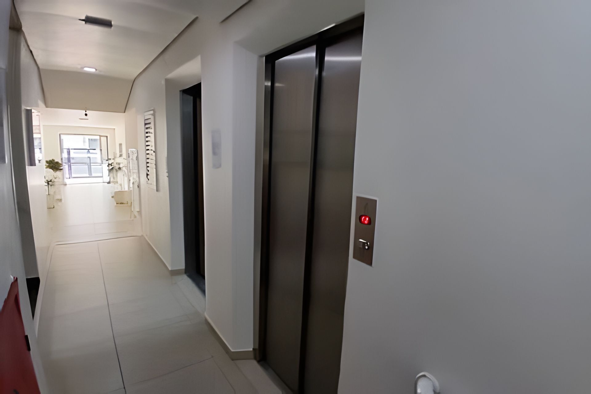 Un pasillo con un ascensor moderno y una puerta que da a una habitación.