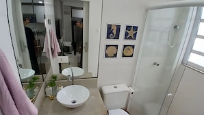 Un baño con lavamanos blanco, inodoro y cabina de ducha de vidrio. Hay cuatro cuadros colgados en la pared.