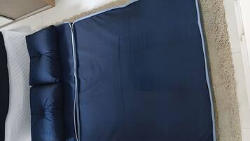 Una cama con un colchón y almohadas azul oscuro, un cabecero blanco y una alfombra texturizada en el suelo.