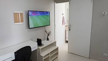 Un espacio de oficina moderno y minimalista con un escritorio blanco, una silla de oficina negra y un televisor de pantalla plana montado en la pared.