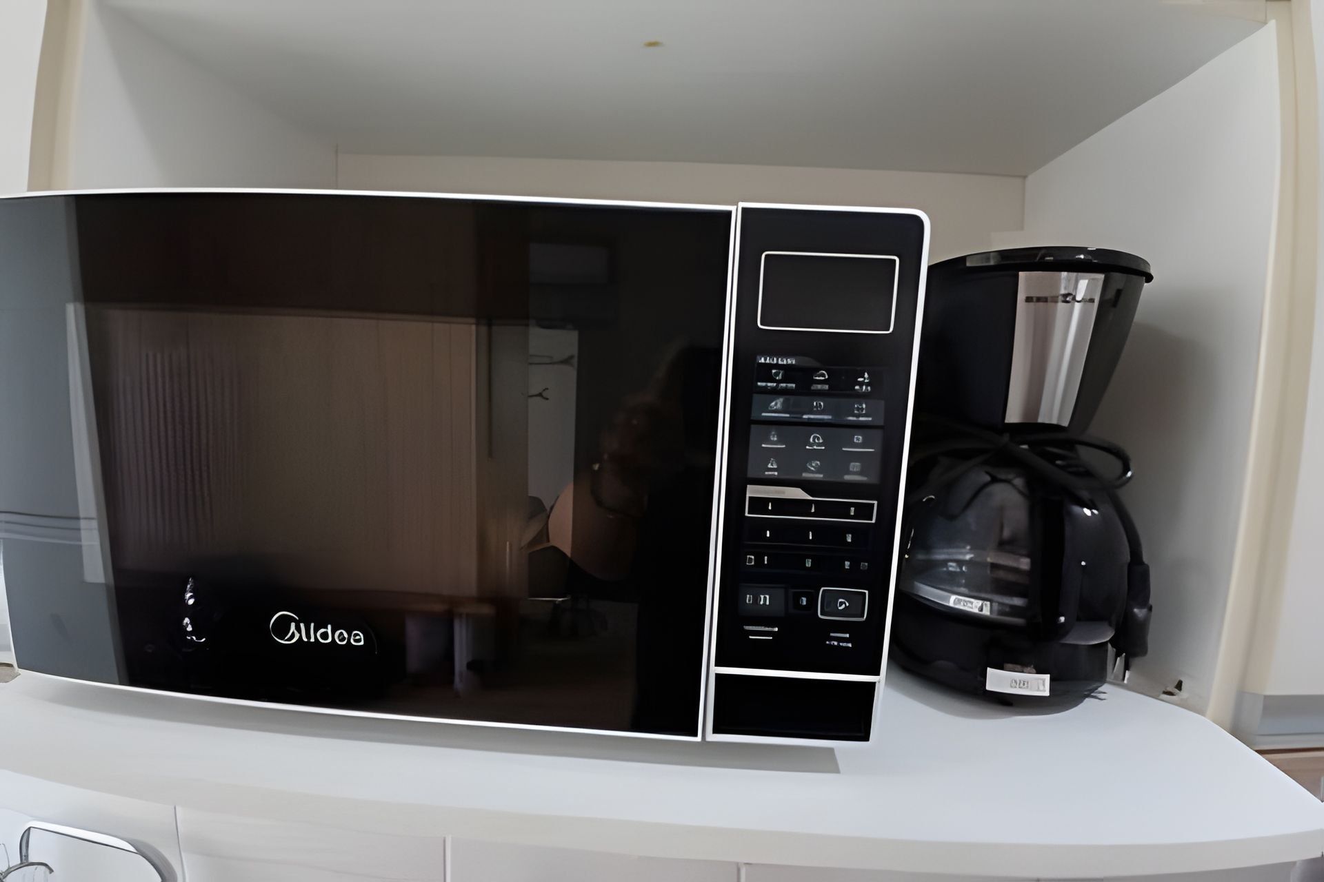 Une cuisine avec un micro-ondes noir et une machine à café posés sur le plan de travail.