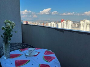 Ein Balkon mit Tisch, Blumen in einer Vase und Blick auf die Stadt.